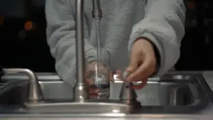 Person zapft Wasser aus Wasserhahn in ein Glas